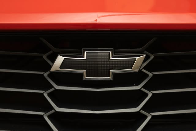Close-up of a Chevrolet badge and grille beneath a red hood