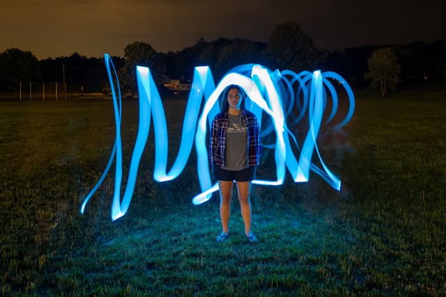 Portrait outdoors at night surrounded by vivid blue light trails